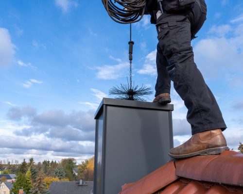 chimney-sweep-cleaning-a-chimney-standing-on-the-house-roof-lowering-picture-id1284524676